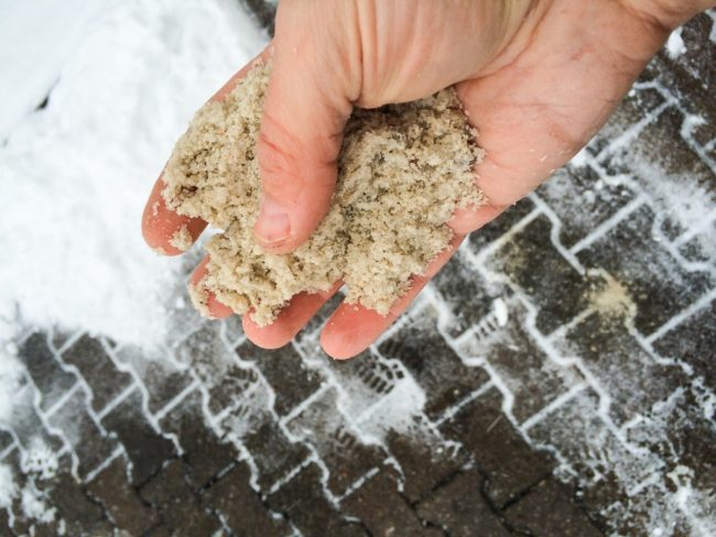 Hand holding deicing sand above the pavement, ready to disperse